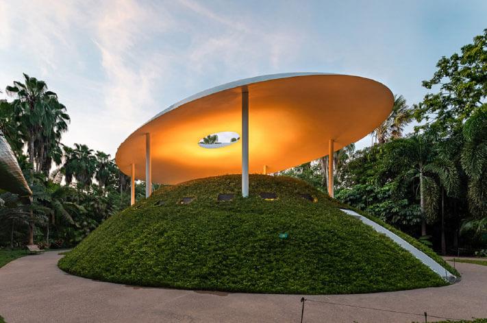 Ein begehbarer Pavillon von Tatiana Bilbao Estudio erhebt sich wie eine bewachsene Skulptur aus dem tropischen Garten – mit einer schwebend wirkenden Dachscheibe, die Licht einfängt und Schatten spendet. Foto: © tatianabilbao.com